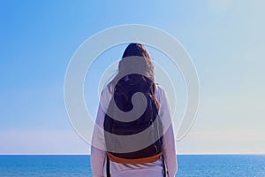 Girl traveller with backpack stands looks at sea on vacation side view outdoor.