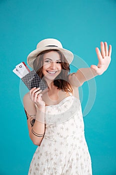 Girl traveller holding passport and travelling tickets and waving goodbye