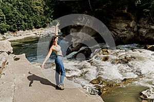 Girl is travelling in Karpathian mountains and feeling freedom. Waterfall in mountain river. Cascade waterfall and