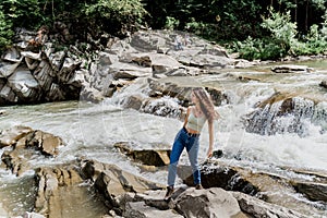 Girl is travelling in Karpathian mountains and feeling freedom. Waterfall in mountain river. Cascade waterfall and