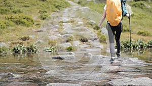 Girl with trekking poles crossing stream in mountains