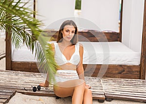 Girl on a tropical beach in white swimsuit and sunglasses posing