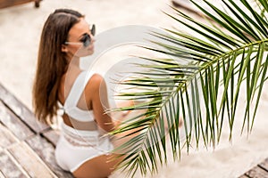 Girl on a tropical beach in white swimsuit and sunglasses posing