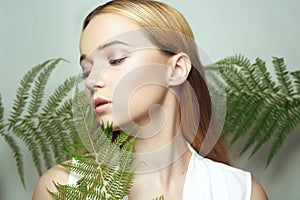 Girl in tropical leaves enjoys eyes closed. Portrait of a beautiful blonde with perfect clean skin. Pink makeup beauty photo, big