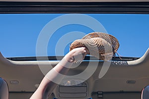 Girl trowing away her straw hat out from open hatch of a vehicle.