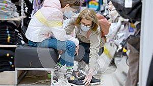 Girl trying on sneakers in supermarket and mother helping