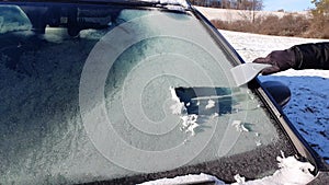 Girl is trying to defrost windscreen by ice scraper in very freezing weather.