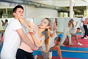 Girl trying to escape rear hug of male opponent, striking with elbow to chin