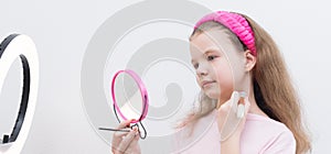 The girl, tucking her hair into a bandage, makes a make-up, looking in a pink mirror, on the left a circular light, close-up