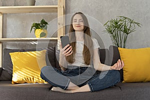 Girl turned on mantra on phone and meditating. Woman sits in lotus position and turns on meditation on her smartphone