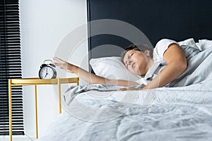 The girl turns off the annoying alarm clock to continue sleeping. Get some more sleep. It a hard morning. Time to wake up