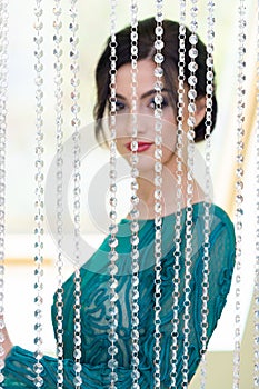 Girl in a turquoise dress standing behind decorative glass curtain. Focus on creeping stones. The girl is blurred