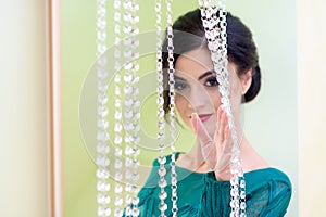 Girl in a turquoise dress standing behind decorative glass curtain. Focus on girl`s hand. The girl is blurred