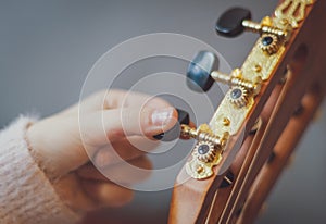 The girl twists the guitar peg while tuning the strings.