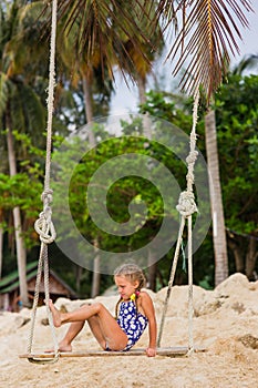 Girl with two braids in a bathing suit on a swing on the beach