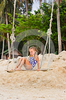 Girl with two braids in a bathing suit on a swing on the beach