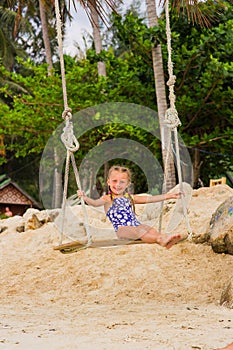 Girl with two braids in a bathing suit on a swing on the beach