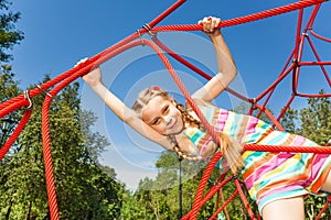 Girl with two braids hangs on ropes of red net