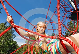 Girl with two braids sits on ropes of red net