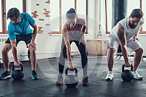 Girl And Two Guys Lifting Weights In Fitness Club photo