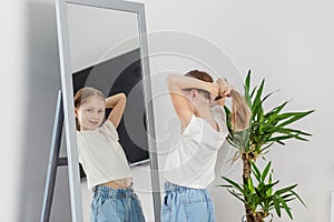 Girl Tying Hair in Front of Mirror. Morning preparation before school