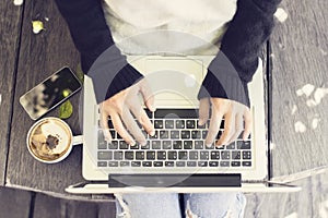 Girl typing a message in laptop with cappuccino and smartphone