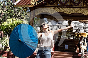 Girl with an umbrella in one hand with open arms in front of a Buddhist temple