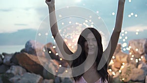 Girl unbridled fun on the background of fireworks. young woman in cocktail dress dancing holding sparklers. portrait of