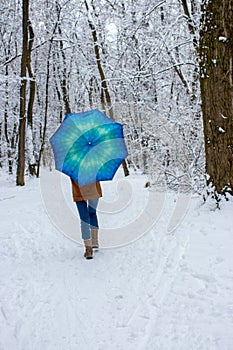 Girl under blue umbrella in snowy forest. Snowfall concept. Woman under wet snow rain in winter park.