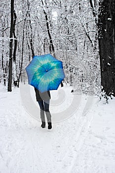 Girl under blue umbrella in snowy forest unfocused. Snowfall concept. Woman under wet snow rain in winter park.