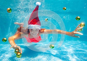 Girl underwater in Santa hat with Christmas balls