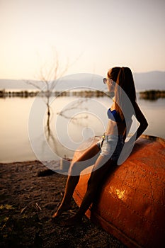 Girl on an upside down rowboat looking at sunset