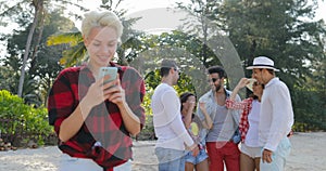 Girl Use Cell Smart Phone Chatting Online Over Young People Group Talking In Tropical Palm Tree Park