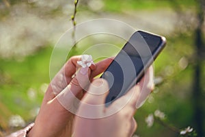 Girl uses her Mobile Phone outdoor, close up. Sunny day. Spring flowers. Beautiful Orchard.