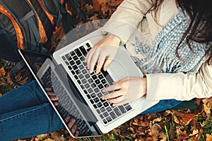 girl uses a laptop while sitting on the grass in the autumn park