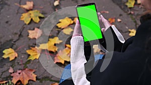 Girl uses a smartphone with a green screen, sitting on a park bench, top view, Technologies on an autumn walk