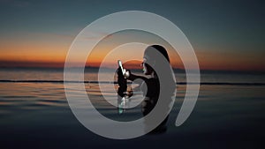 Girl uses smartphone in the pool at sunset