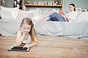 Girl using digital tablet with mother reading book