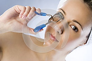 Girl using eyelash curler and makes eyelashes wider