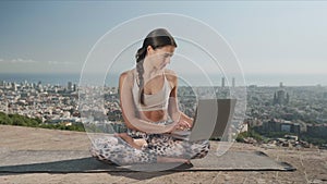 Girl using laptop in city of Barcelona. Yoga woman sitting in lotus pose on mat