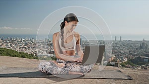Girl using laptop in city of Barcelona. Yoga woman sitting in lotus pose on mat