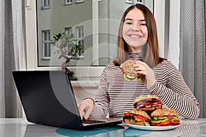 Girl using a laptop and eating a vegetarian sandwich at home