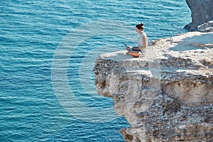 Girl using laptop for work. Sea and nature landscape from high cliff. Travelling and remote office concept, copy space