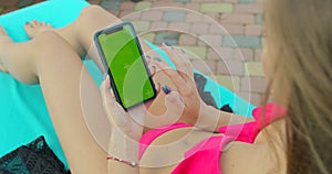 Girl using mobile phone green screen near the swimming pool. Hands holding smartphone chrome key, fingers tapping modern