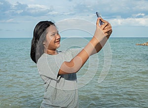 A girl using a phone to take a selfie on a sea background