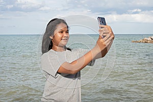 A girl using a phone to take a selfie on a sea background