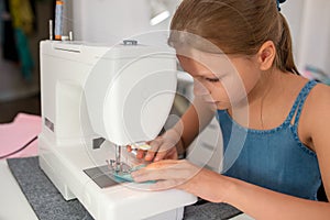 Girl using a sewing machine to sew on a piece of fabric. Creative tailoring workshops for children