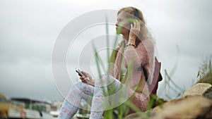 A girl using a smartphone on the beach, listening to music in headphones, dancing a yacht and sailing in the harbor.