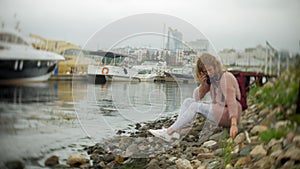 A girl using a smartphone on the beach, listening to music in headphones, dancing a yacht and sailing in the harbor.