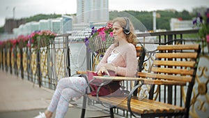 A girl using a smartphone on a bench in flowers on the beach, listening to music in headphones, dancing a yacht and